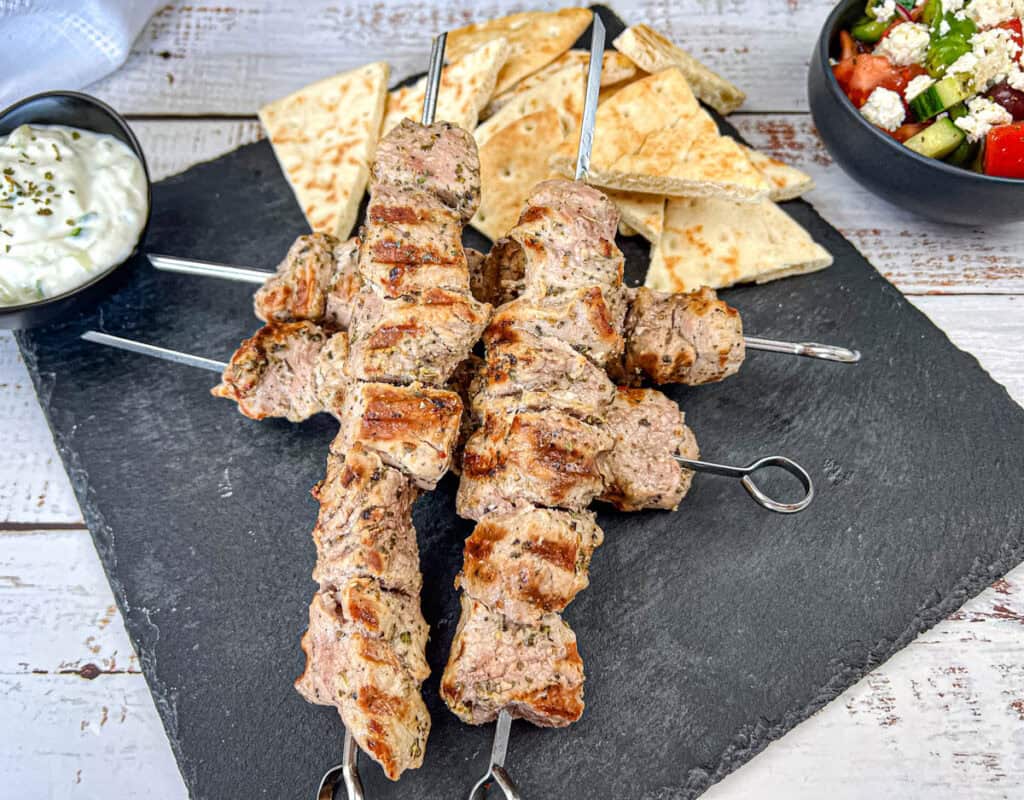 Pork souvlaki on a black slate plate with pita bread.