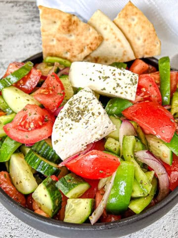 Bowl of Horiatiki Salad with feta cheese on top and pita bread on the side.