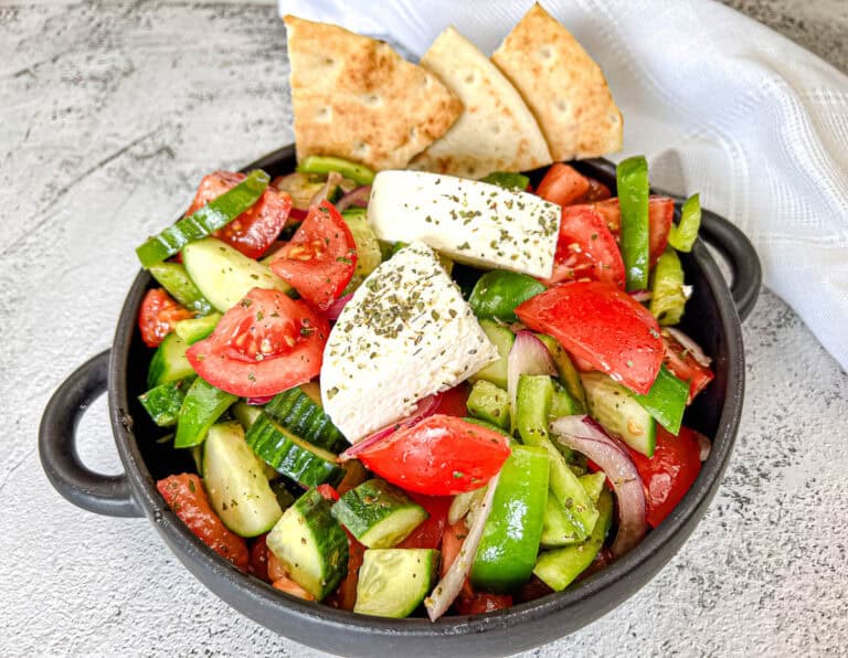 A bowl of Horiatiki salad topped with feta cheese, served with pita bread on the side.