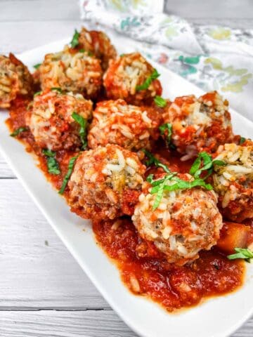 A plate of Slow Cooker Porcupine Meatballs with fresh basil on top.