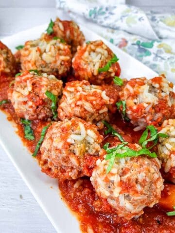 A plate of porcupine meatballs covered in tomato sauce and garnished with fresh basil.