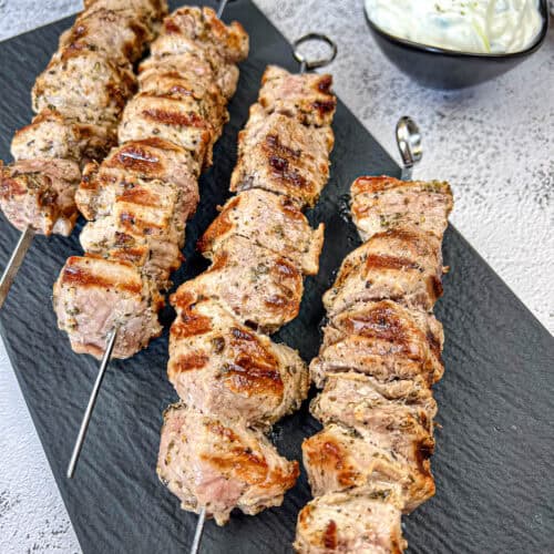 Four pieces of pork souvlaki on a slate plate.