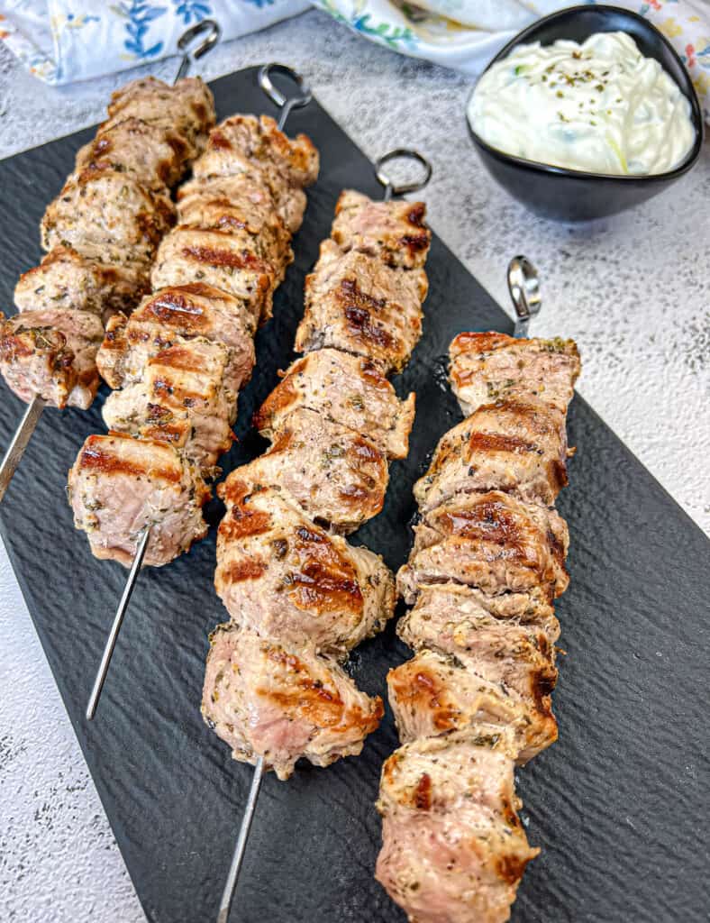 Four pieces of pork souvlaki on a slate plate.