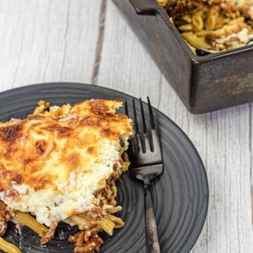 Pastitsio on a black plate beside the tray.