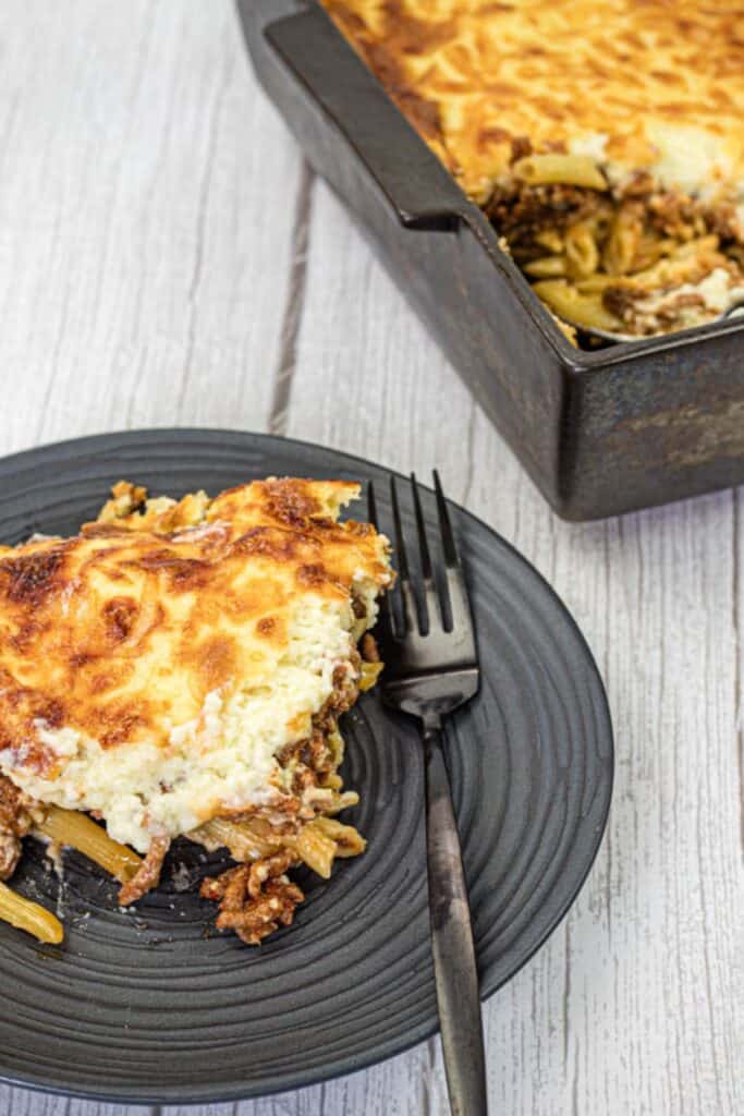 Pastitsio on a black plate beside the tray.