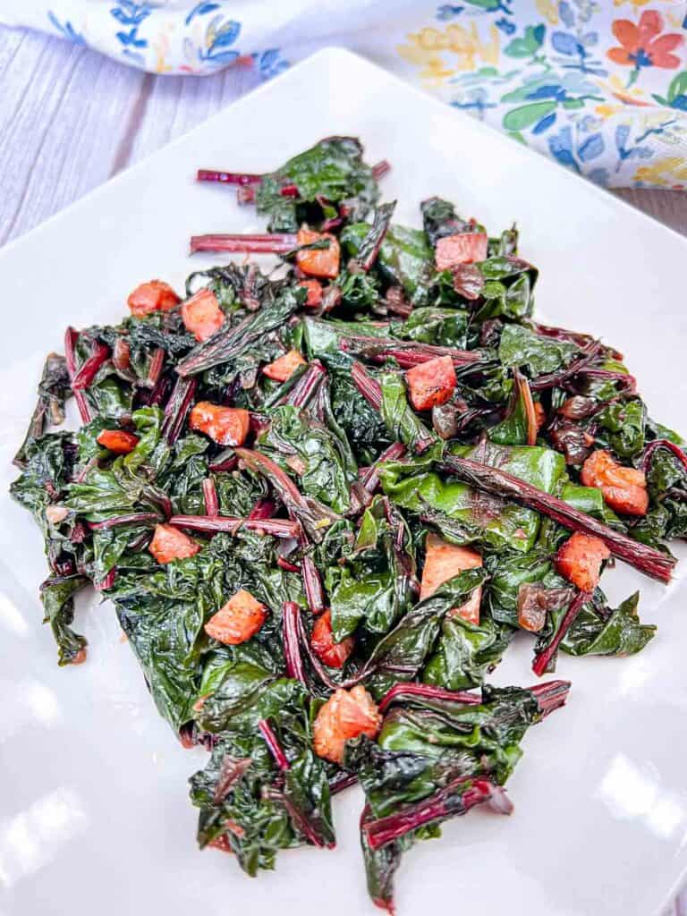 Sauteed Beet Greens with Pancetta served on a white plate.