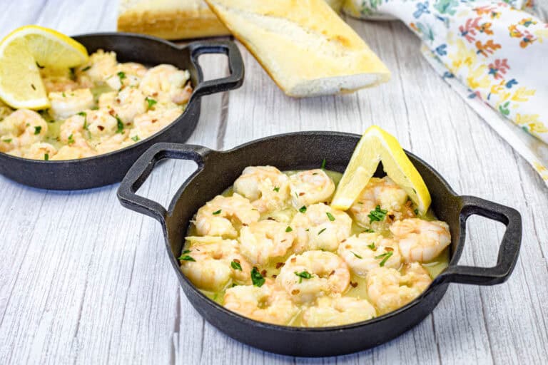 Shrimp scampi with a lemon slice on a black dish.