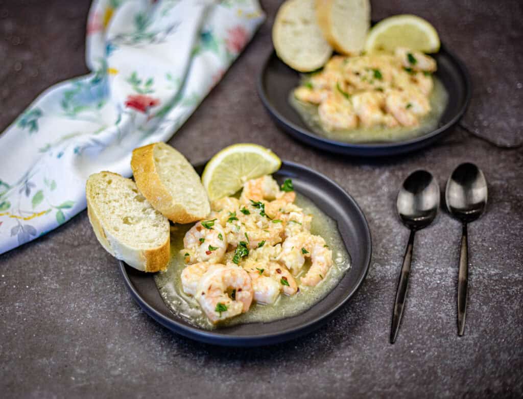 A plate of Shrimp scampi with two spoons beside.