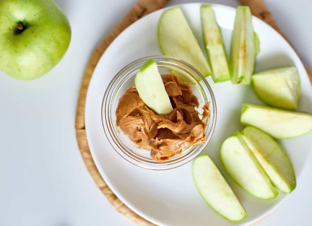 Green slices apples with peanut butter on white background.