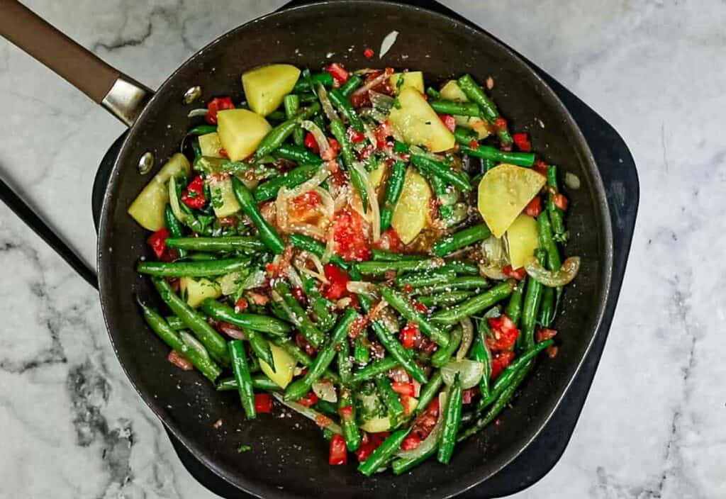 Stir in the trimmed and cut green beans, grated tomato, and garlic and mix well. 