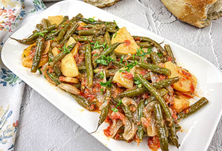 Greek green beans served on a white rectangular plate.