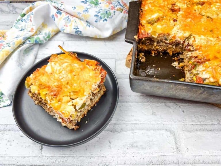 A slice of John Wayne casserole on a black plate beside the pan.