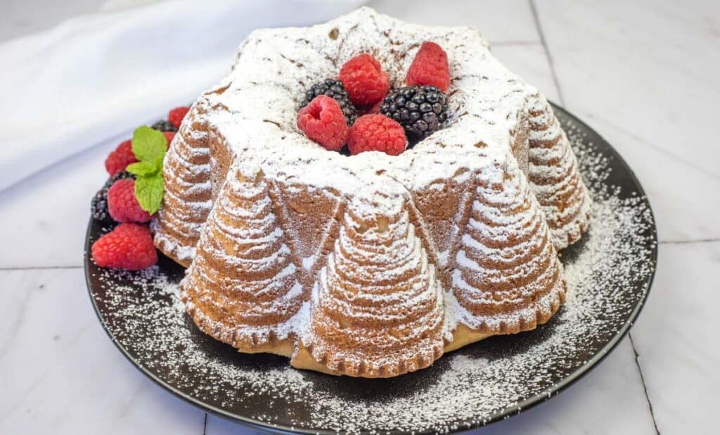 Old Fashioned Whipped Cream Cake with powdered sugar and fruits on a plate.