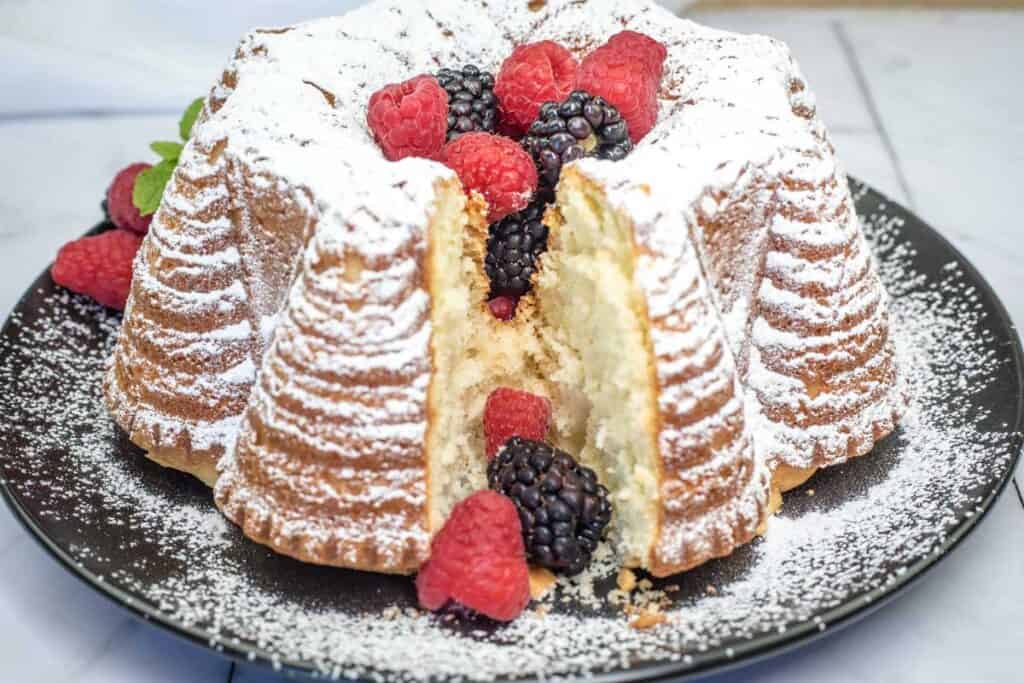 A plate of Old Fashioned Whipped Cream Cake with berries and powdered sugar.