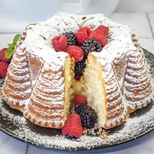 Old Fashioned Whipped Cream Cake with a small slice topped with powdered sugar and berries.