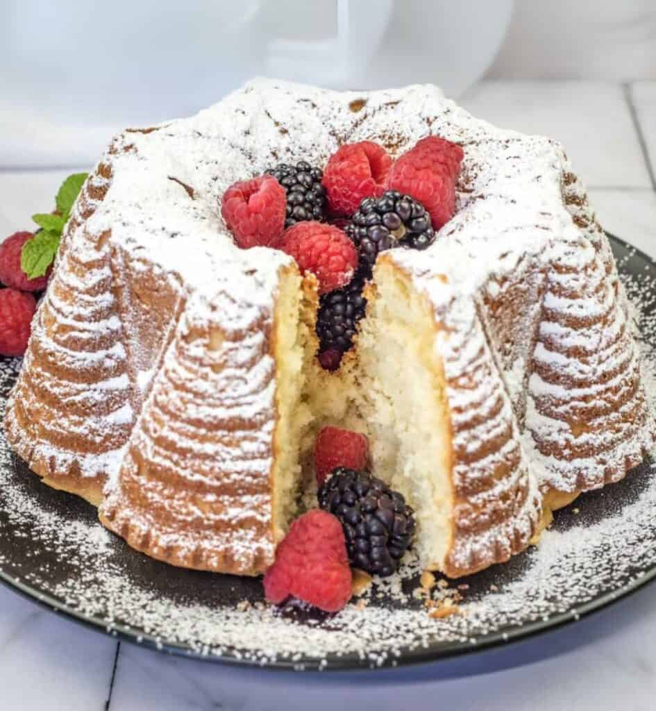 Old Fashioned Whipped Cream Cake with a small slice topped with powdered sugar and berries.