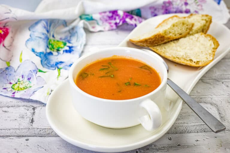 A bowl of old-fashioned tomato soup served with a slice of bread on the side.