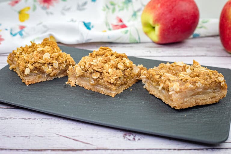 Three pieces of Dutch apple pie squares on a black slate plate.