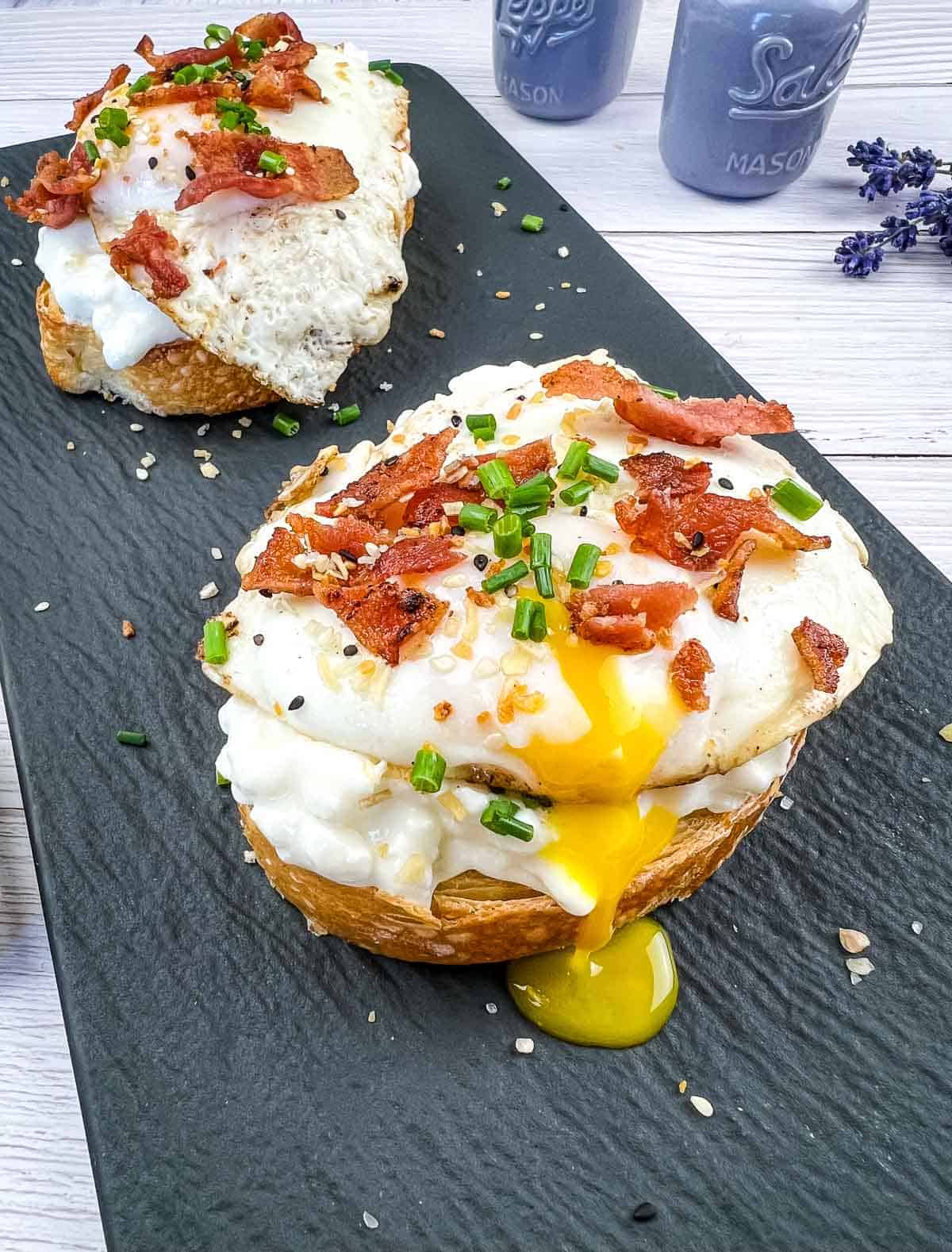 Two pieces of Cottage Cheese Toast with Bacon & Poached Egg on a slate plate.