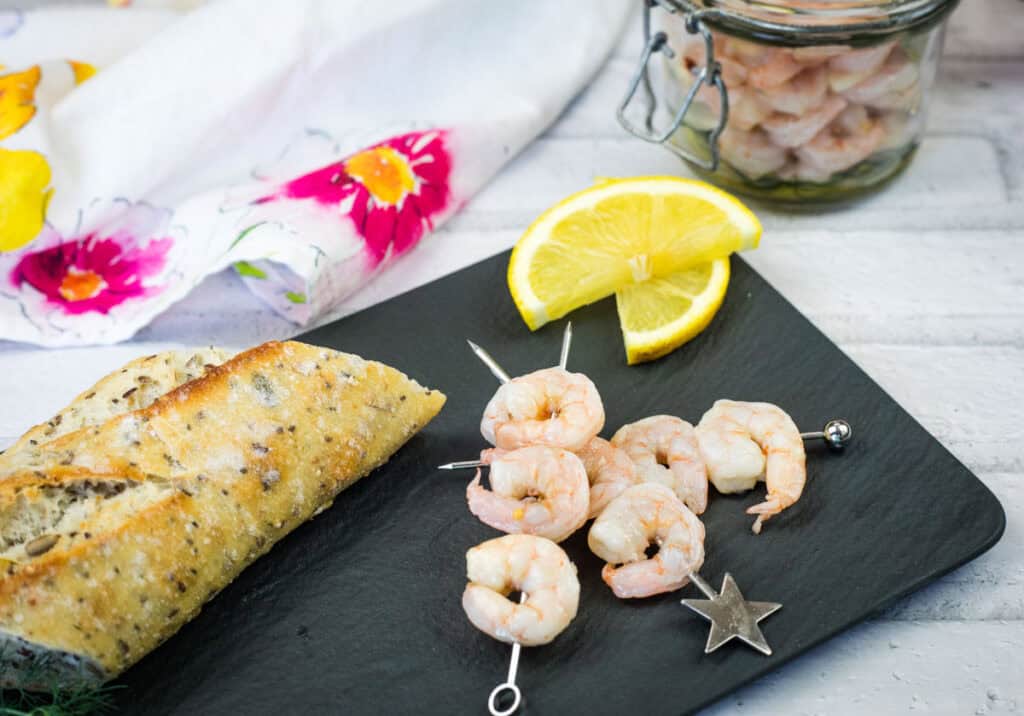 Southern Style Pickled Shrimp on mall skewers with lemon slices on a plate.
