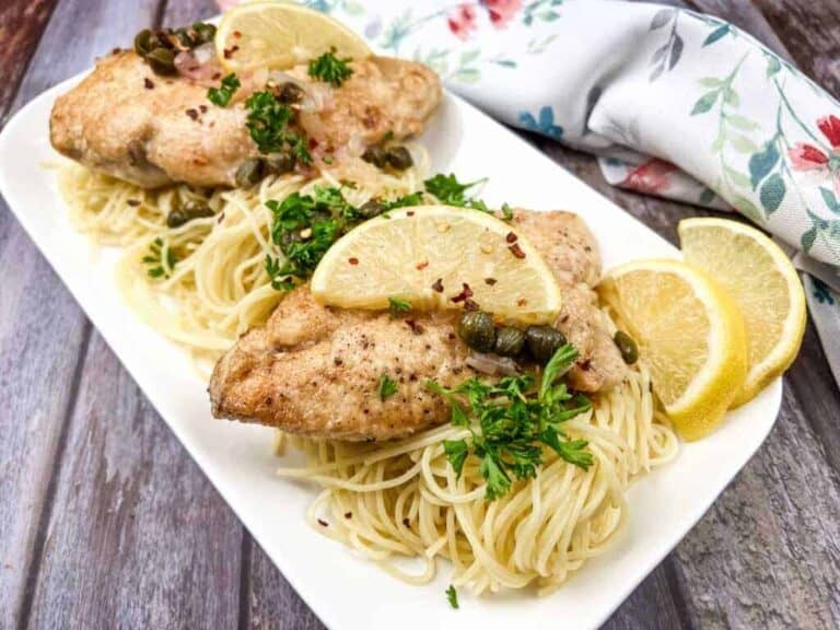 Chicken Piccata served over pasta, garnished with lemon slices, capers, and parsley.