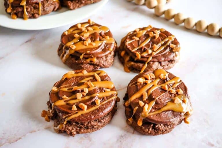 Chocolate Caramel Cookies.Chocolate Caramel Cookies with frosting, caramel drizzle, and chopped nuts on a white marble surface.