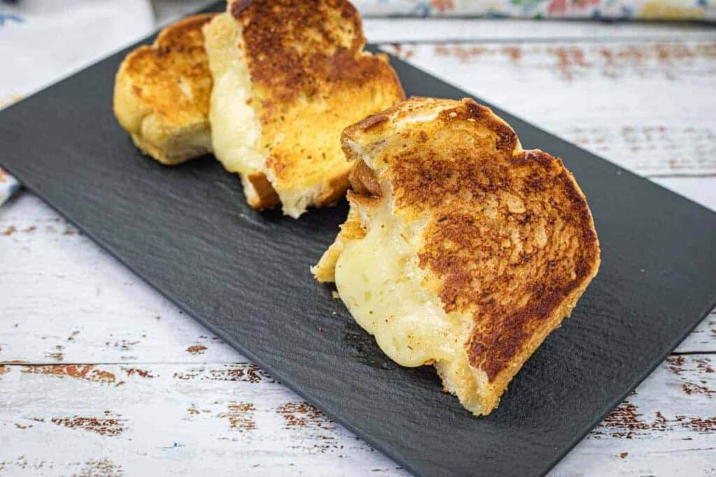 A slate plate with a pieces of The Ultimate Garlic Bread Grilled Cheese.