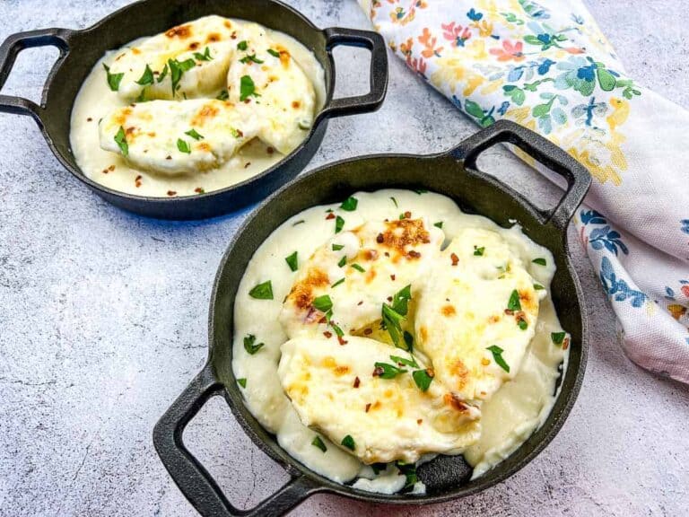 Two cast-iron skillets with baked ricotta cheese garnished with herbs. A floral napkin lies beside them on a light textured surface.