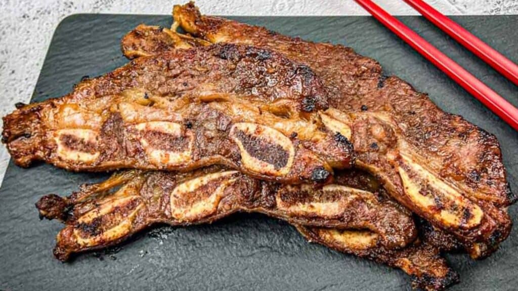 Korean Galbi Ribs on a slate platter with red chopsticks beside them.