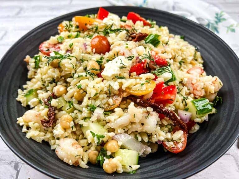 A plate of mixed salad featuring bulgur, chickpeas, cherry tomatoes, cucumbers, red onions, feta cheese, and herbs, served on a black dish.