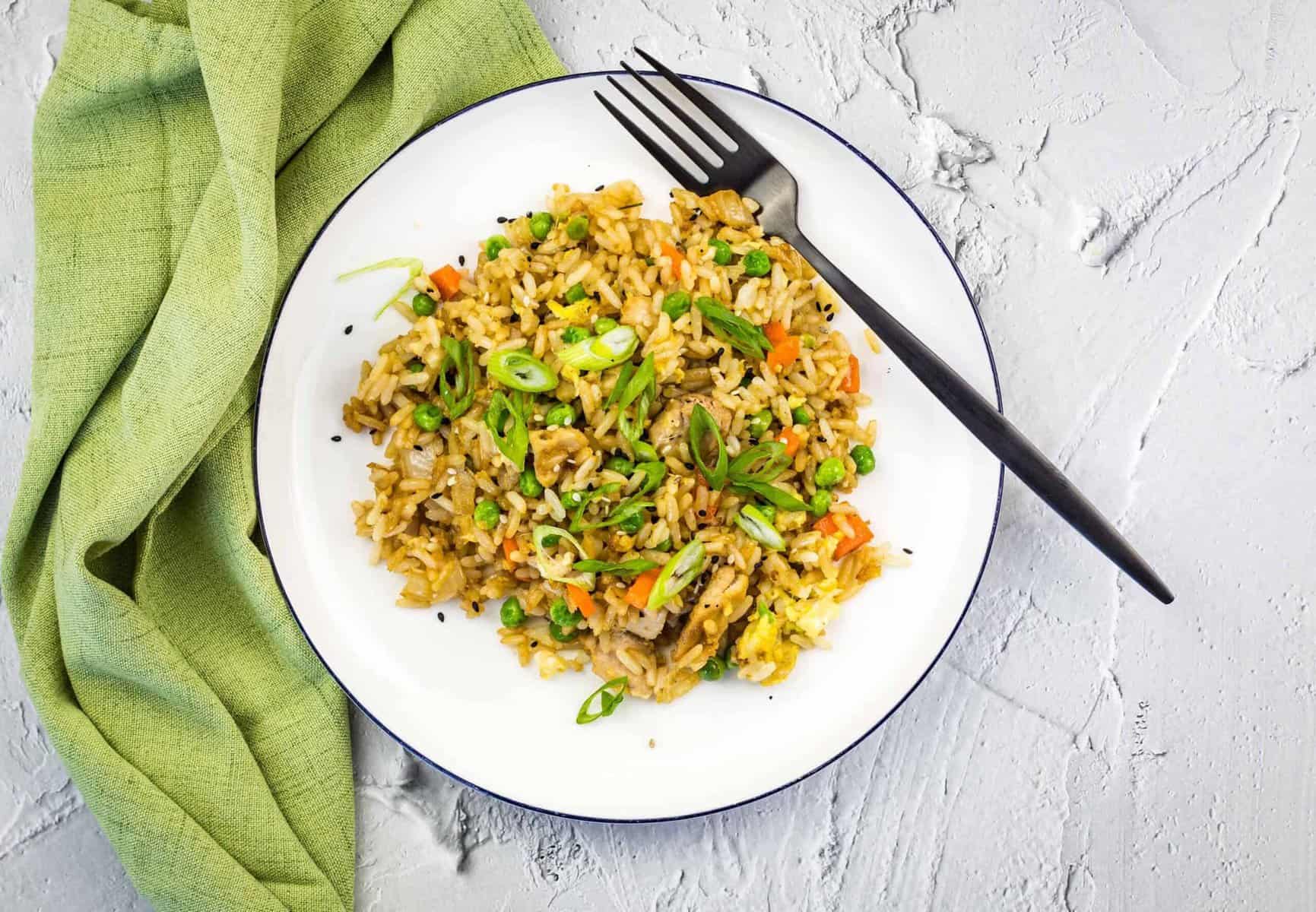 Chicken fried rice on a white plate with a green napkin.