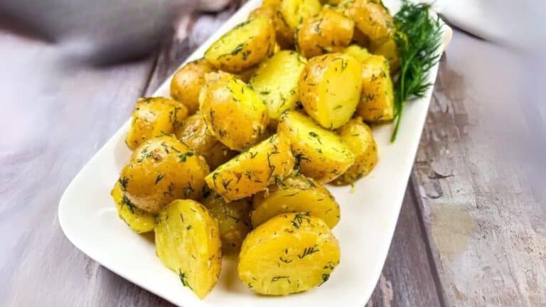 A rectangular white plate with roasted potato pieces garnished with dill.
