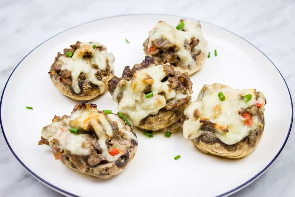 A plate with five stuffed mushrooms topped with melted cheese and garnished with chopped chives.