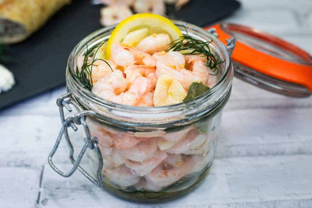 Open jar filled with Southern Style Pickled Shrimp, dill, lemon slices, and herbs.