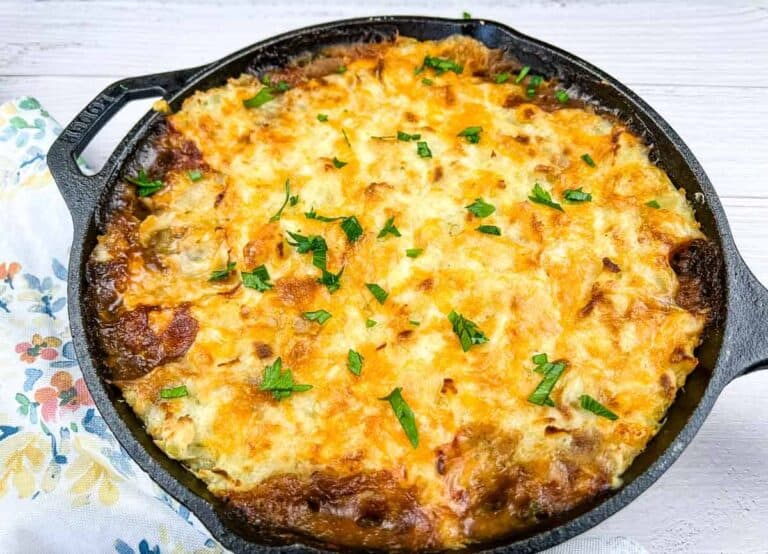 A skillet filled with baked shepherd's pie, topped with melted cheese and garnished with parsley.