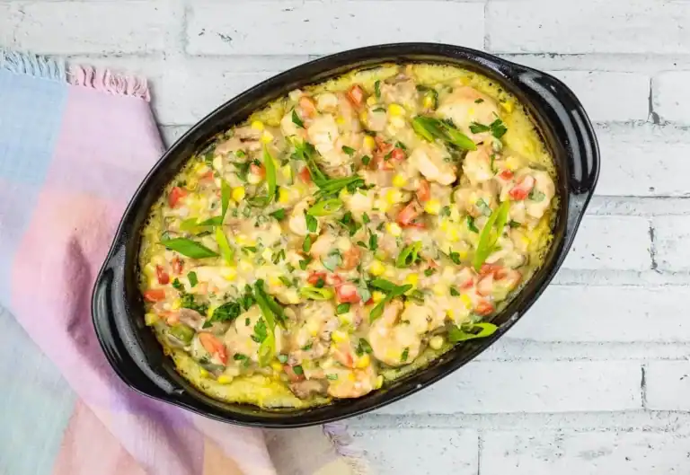 Oval casserole dish filled with a shrimp and vegetable bake topped with chopped herbs, placed on a pastel-colored cloth.