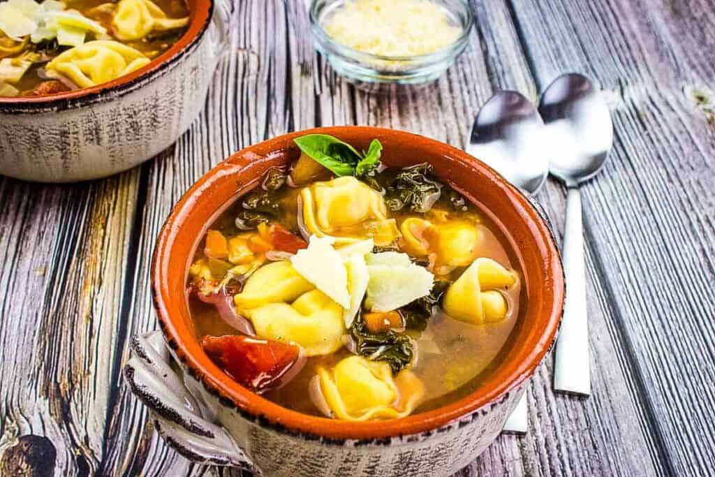 Tortellini Soup with Kale & Chicken in a bowl on a wooden table.