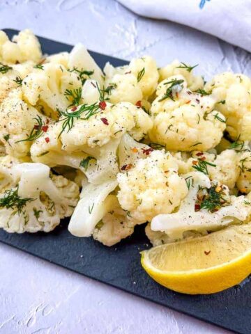 Cauliflower with lemon and dill on a black board.