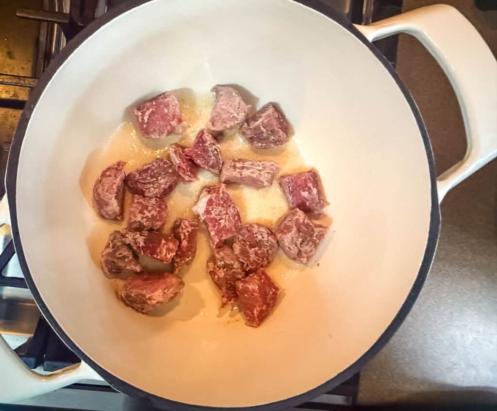 A pot on a stove filled with beef, simmering as it cooks in batches for a hearty meal.