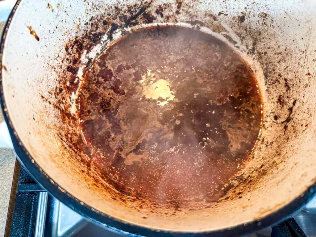 A pot of rich brown liquid simmering on the stove, deglazing with red wine for enhanced flavor.