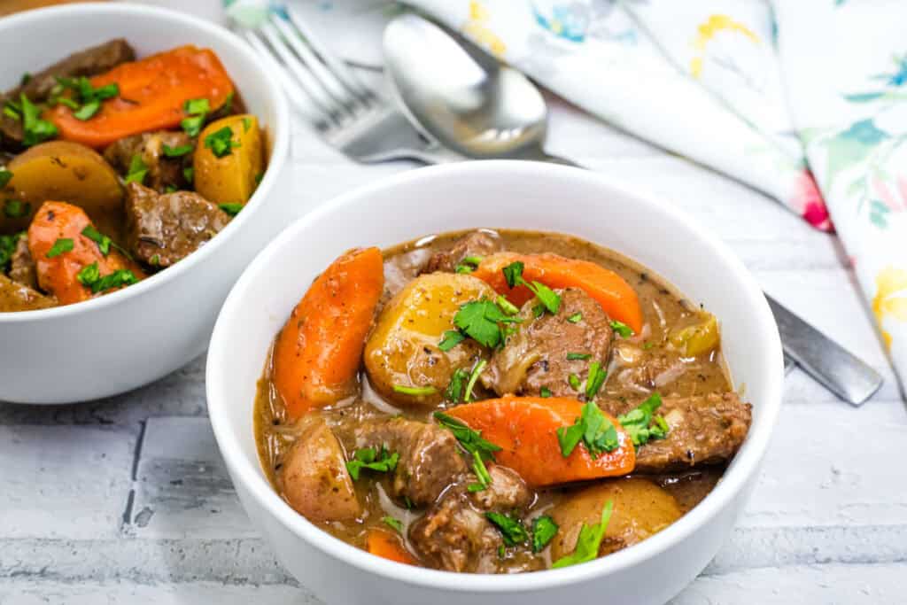 Two bowls of hearty beef stew filled with tender carrots and potatoes, garnished for a comforting meal.