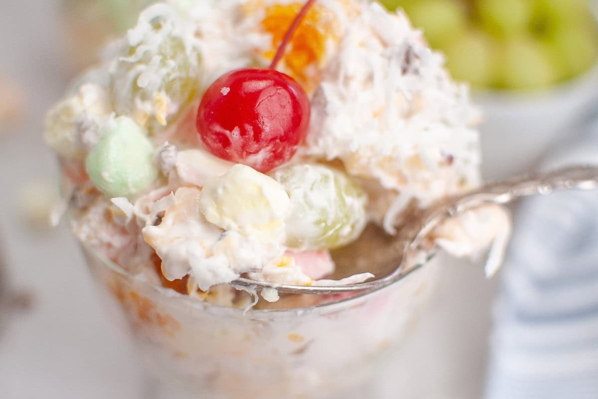 Glass of Ambrosia Salad with fruits and a serving spoon.