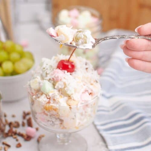 Hand holding a spoon above a bowl of colorful Ambrosia Salad.