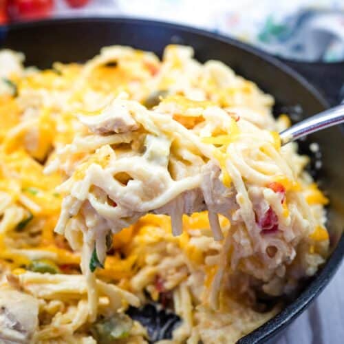 A fork with a serving of chicken spaghetti from a cast-iron skillet.