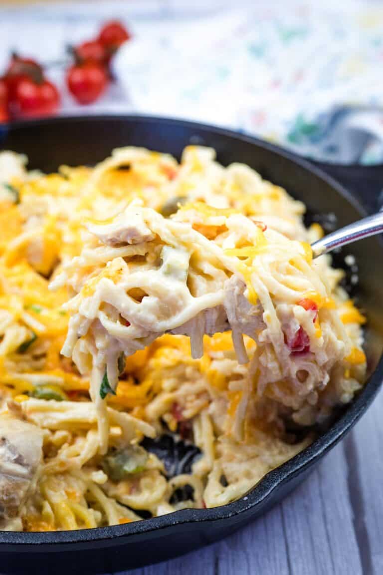 A fork with a serving of chicken spaghetti from a cast-iron skillet.