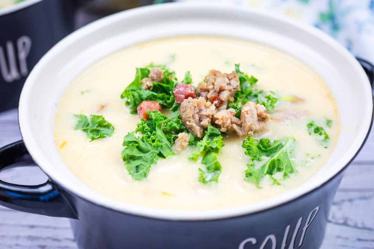 A bowl of Tuscan soup with sausage topped with kale and pancetta pieces in a black soup bowl.