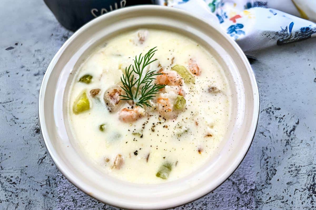 A bowl of fully loaded seafood chowder garnished with fresh dill and cracked pepper on top.