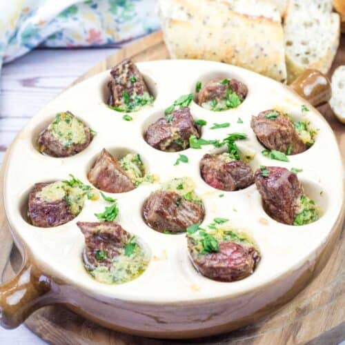 Another image of a Garlic Butter Steak Bites and bread served in an escargot dish on a wooden board.