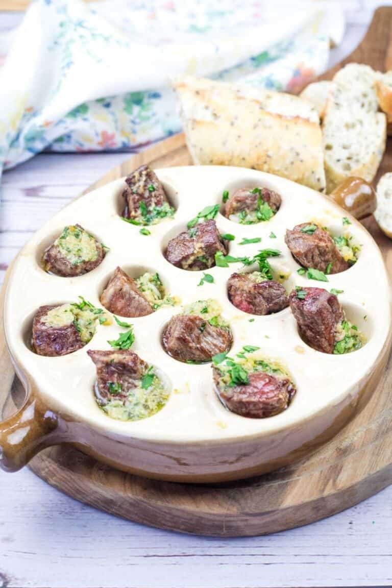 Another image of a Garlic Butter Steak Bites and bread served in an escargot dish on a wooden board.