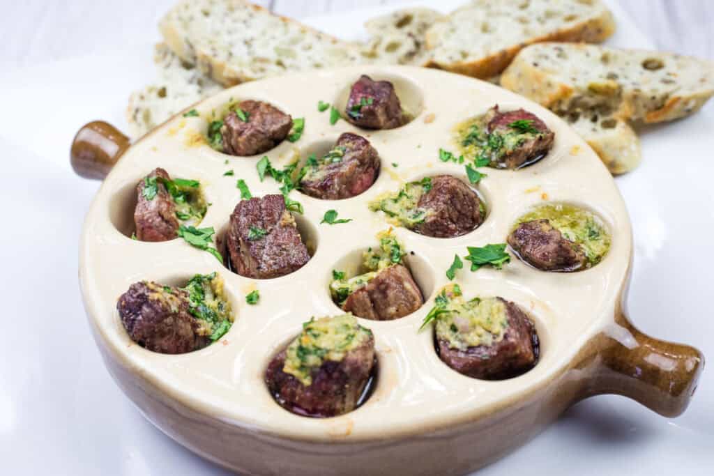 A bowl of garlic butter steak bites and bread on a white plate.